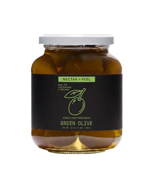 A glass jar of Nectar + Peel Green Olive whole fruit preserves with a black label and white lid, set against a plain white background.